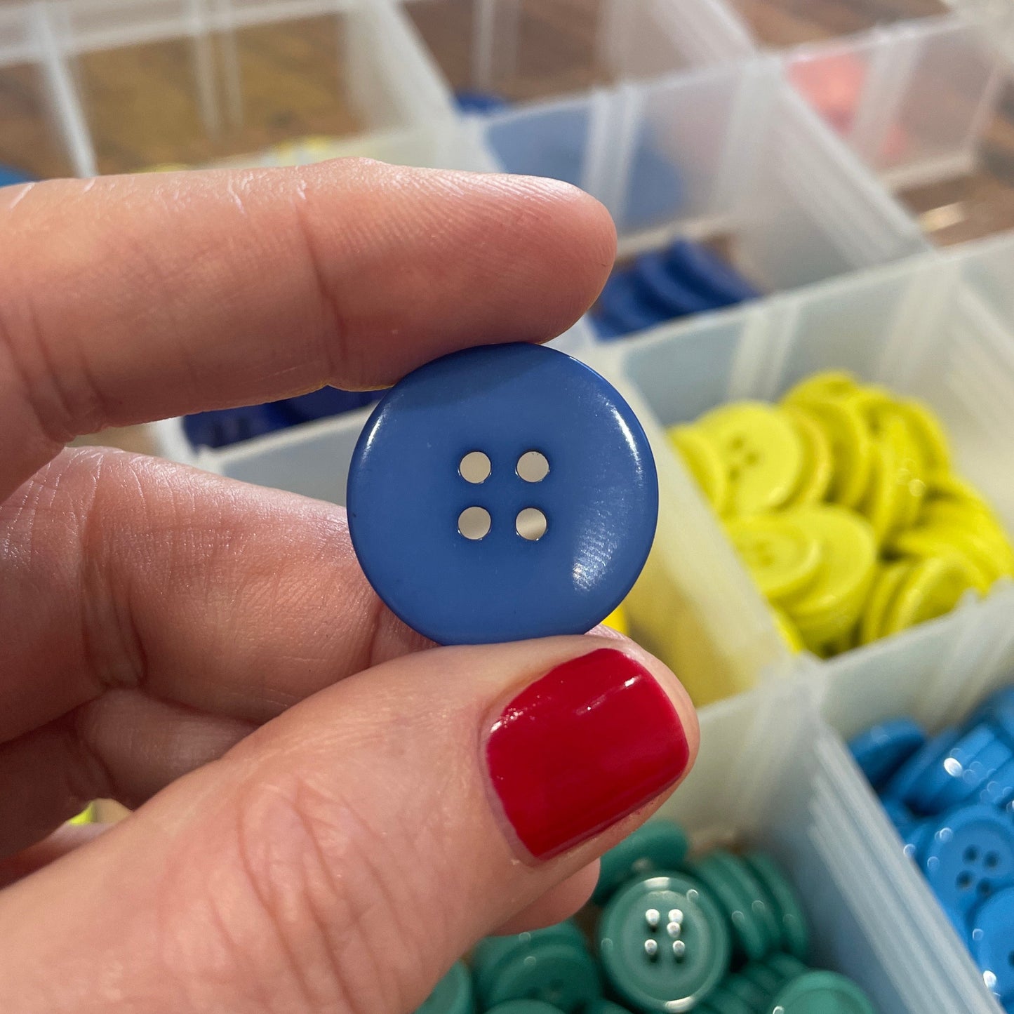 Hand holding a blue button with a blurred background of button containers.