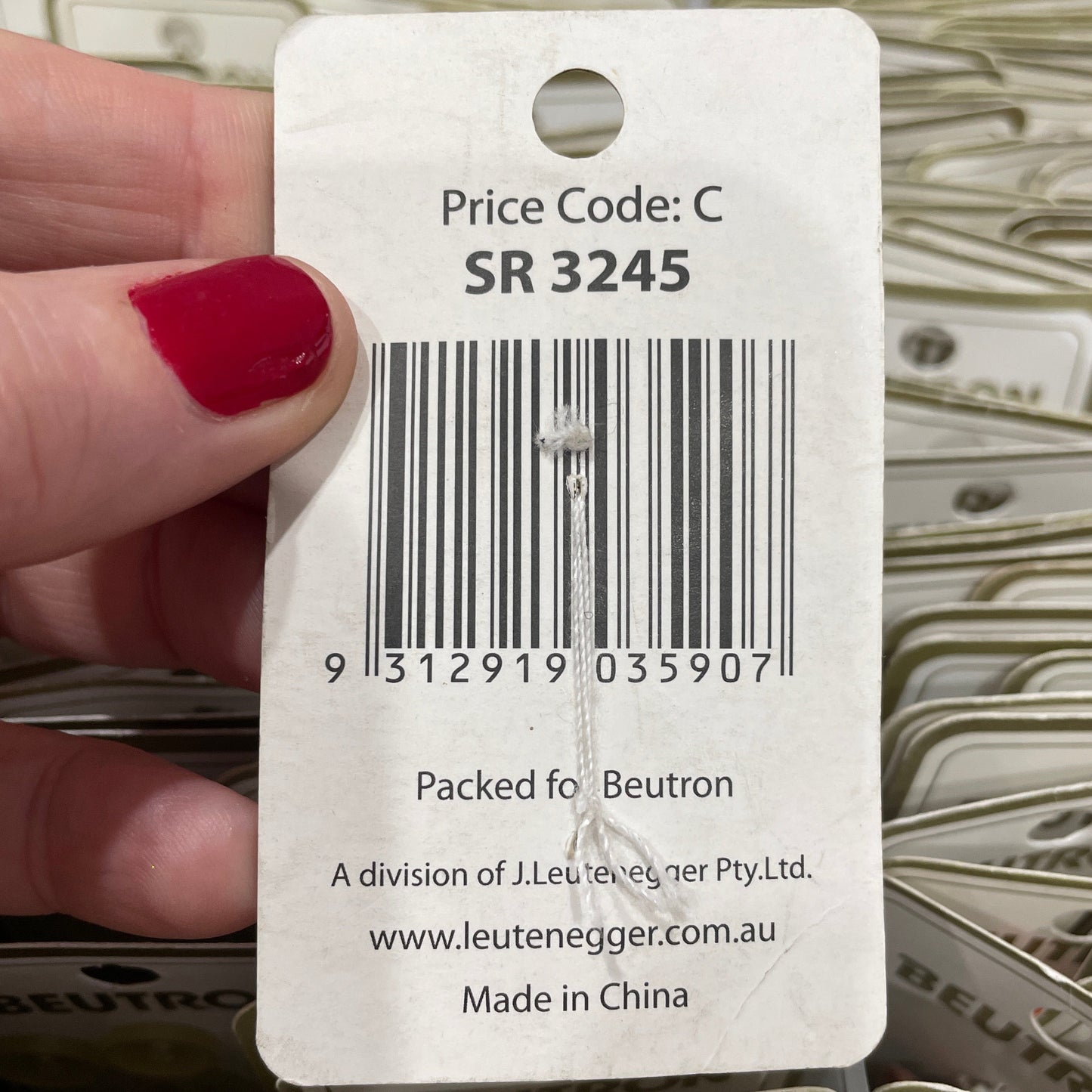 Close-up of a product tag with a barcode and text, held by a hand with red nail polish.