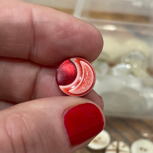 Hand holding a pair of BUTTONS with a clear container of buttons in the background