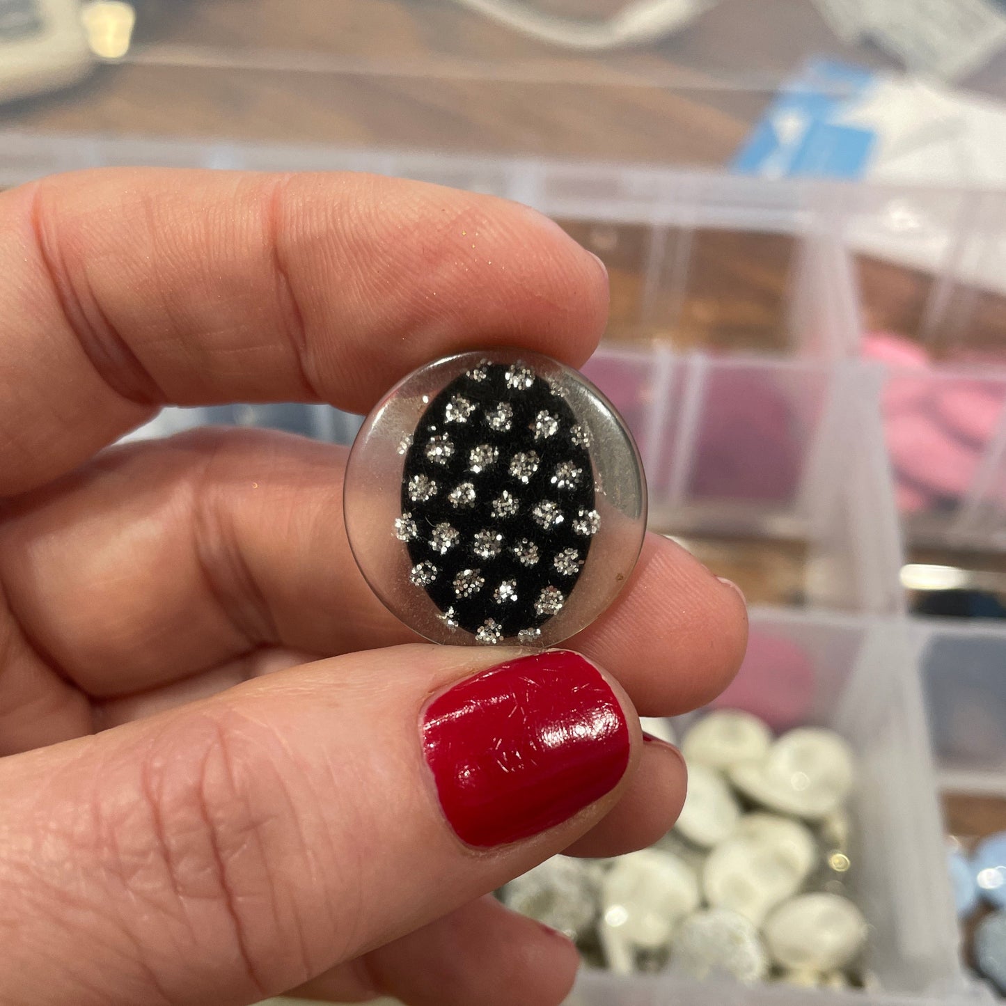 Hand holding a button with black and silver design against a background of colorful buttons.