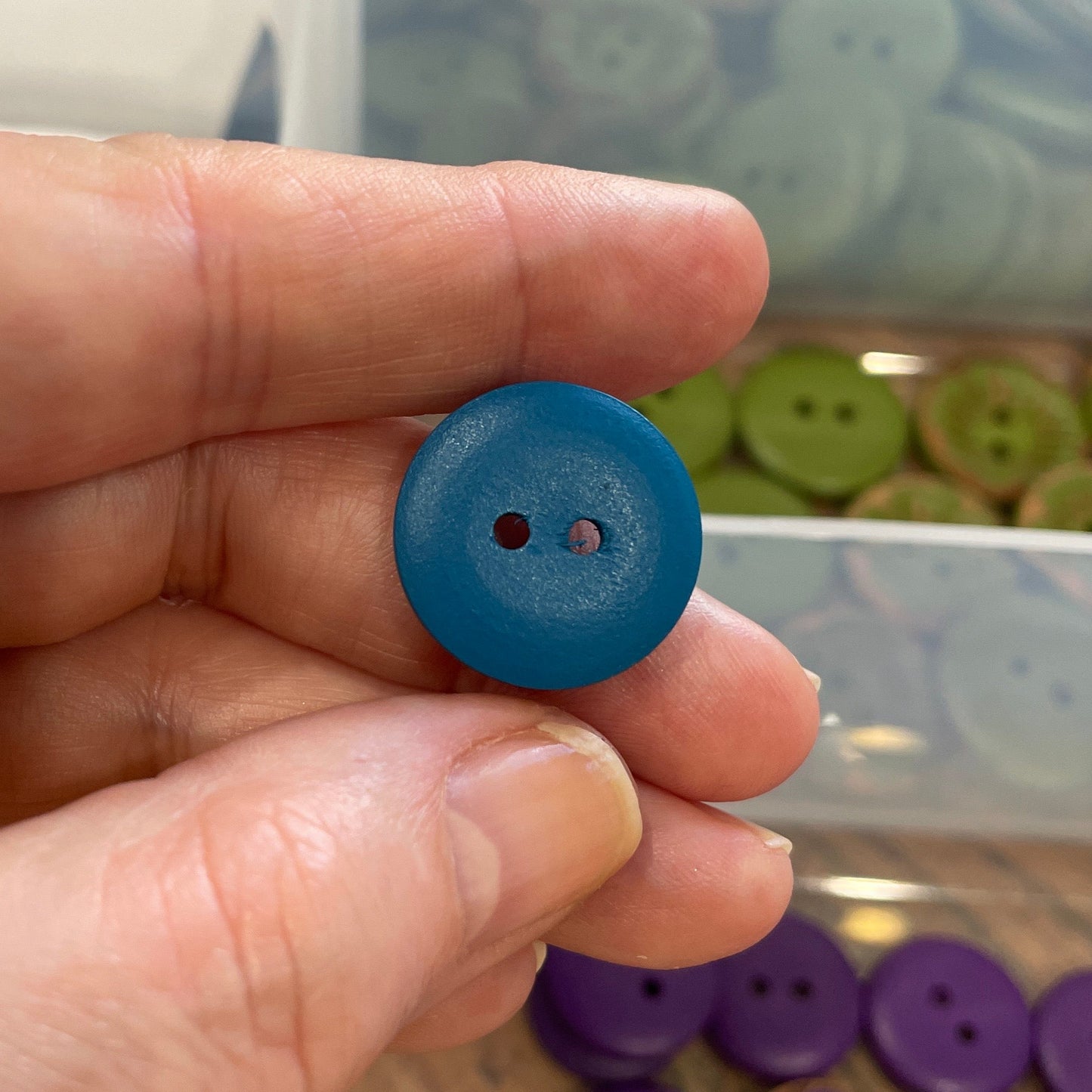 Hand holding a blue button with a background of various buttons in a container.