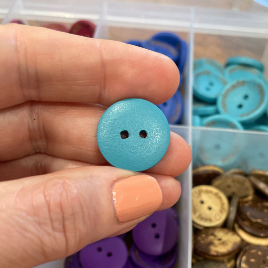 Hand holding a blue button with a container of assorted buttons in the background