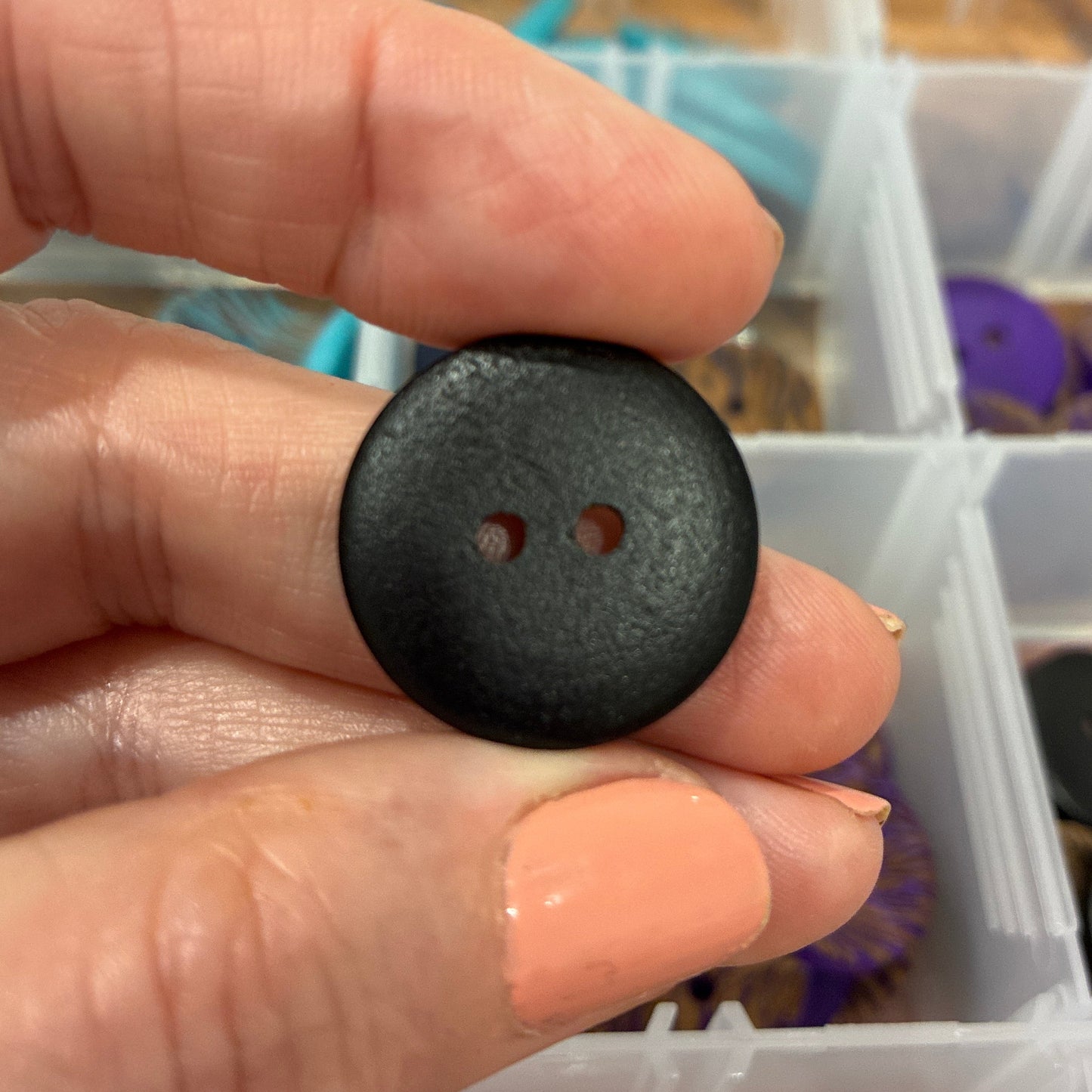Hand holding a black button with a container of buttons in the background