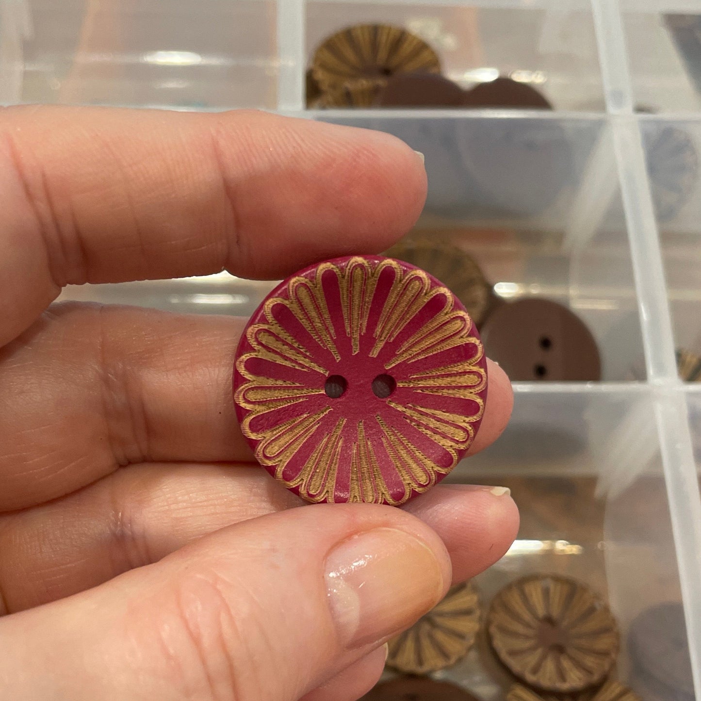 Hand holding a decorative button with a container of various buttons in the background