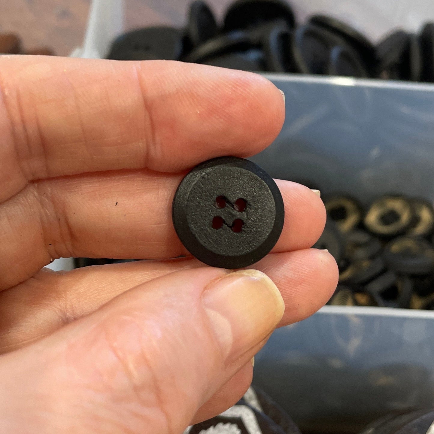 Person holding a black button with a blurred background of buttons and containers.