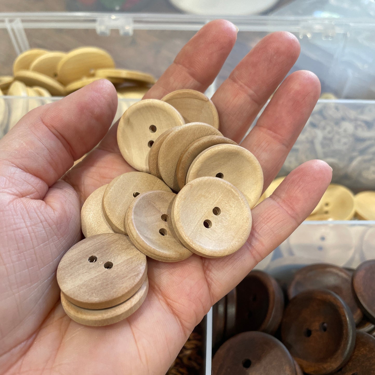 Hand holding a collection of wooden buttons with a blurred background of more buttons.