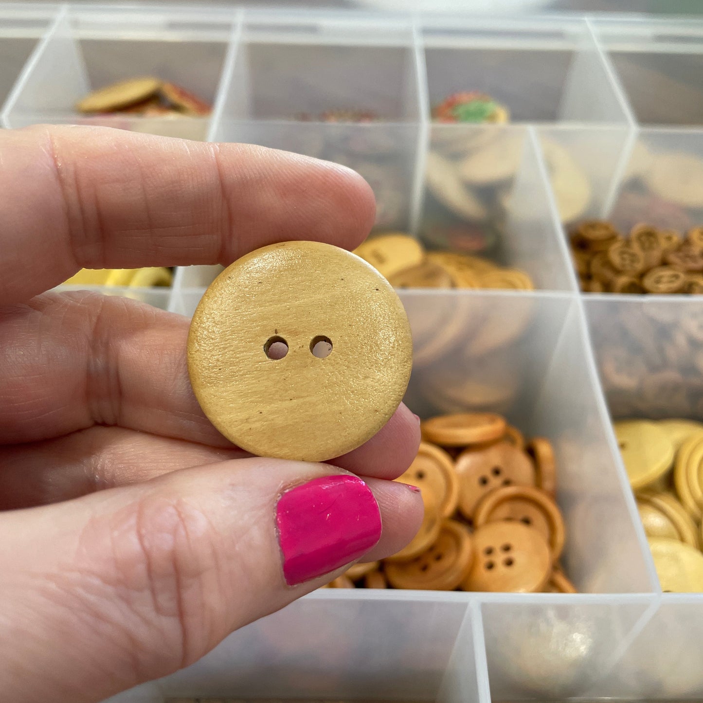 Hand holding a gold button in front of a container of various buttons