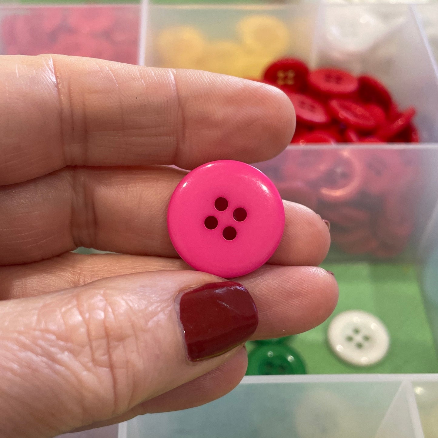 Hand holding a pink button with a background of colorful buttons in a container