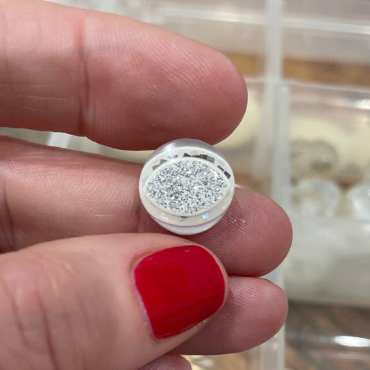 Hand holding a silver earring with a clear gemstone against a blurred background of jewelry.