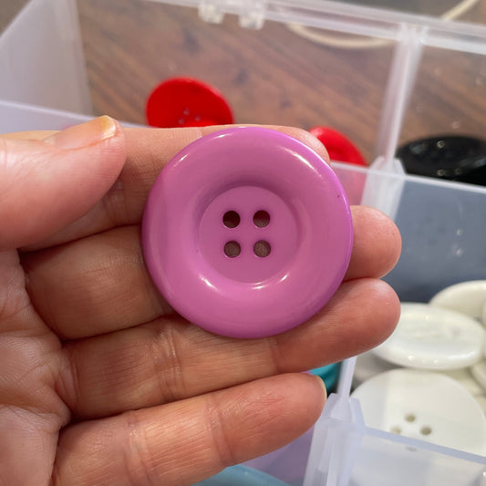 Hand holding a pink button with a blurred background of sewing supplies