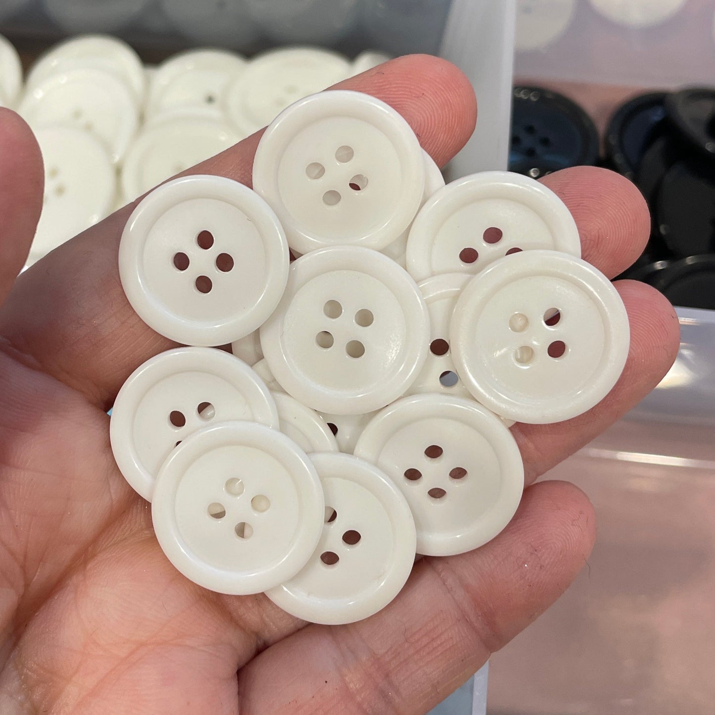 Hand holding white buttons with a container of black buttons in the background