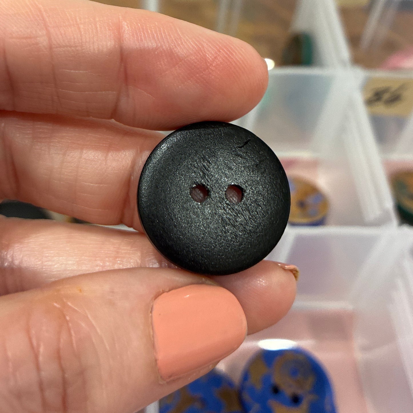 Black button held between fingers with a background of colorful buttons in a case.