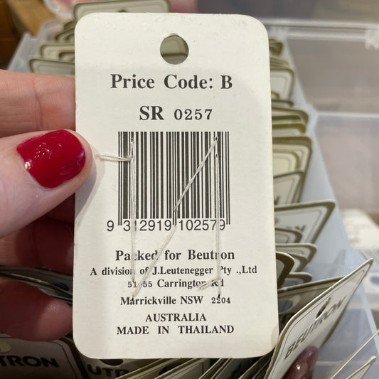 Close-up of a price tag with a barcode and text, held by a hand with red nail polish.