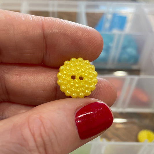 Yellow button held between fingers with a blurred background of buttons