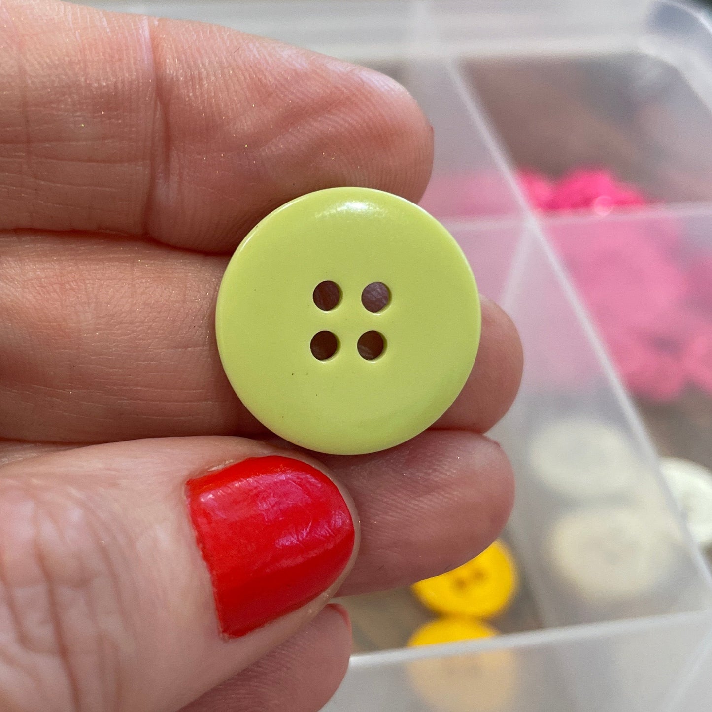 Hand holding a green button with a clear container of buttons in the background
