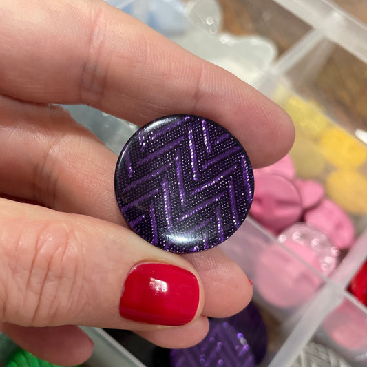 Hand holding a purple textured button with a container of various buttons in the background