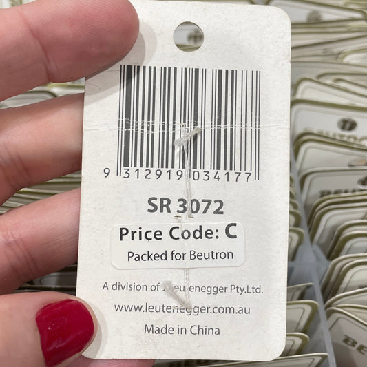 Hand holding a tag with a barcode and text, with a background of more tags.
