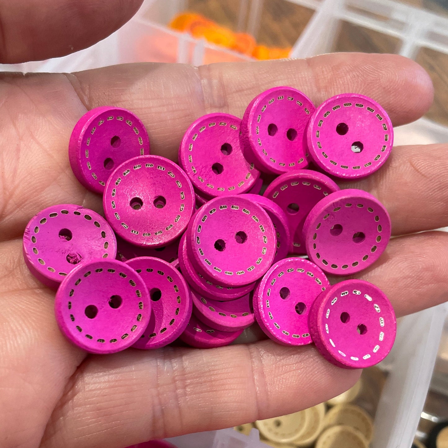 Hand holding pink buttons with a container of more buttons in the background