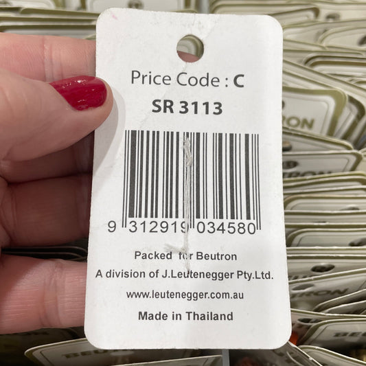 Hand holding a product tag with a barcode and text, with packaging in the background