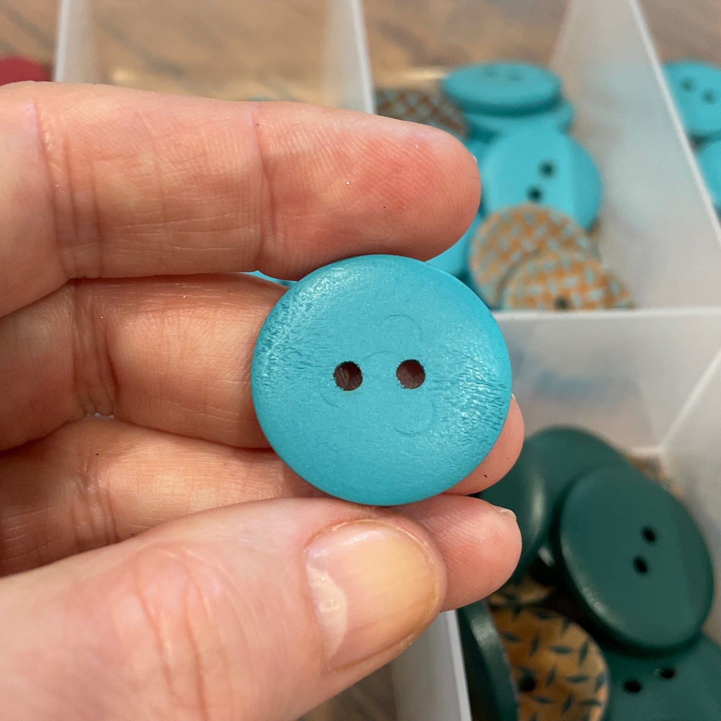 Hand holding a blue button with a container of buttons in the background