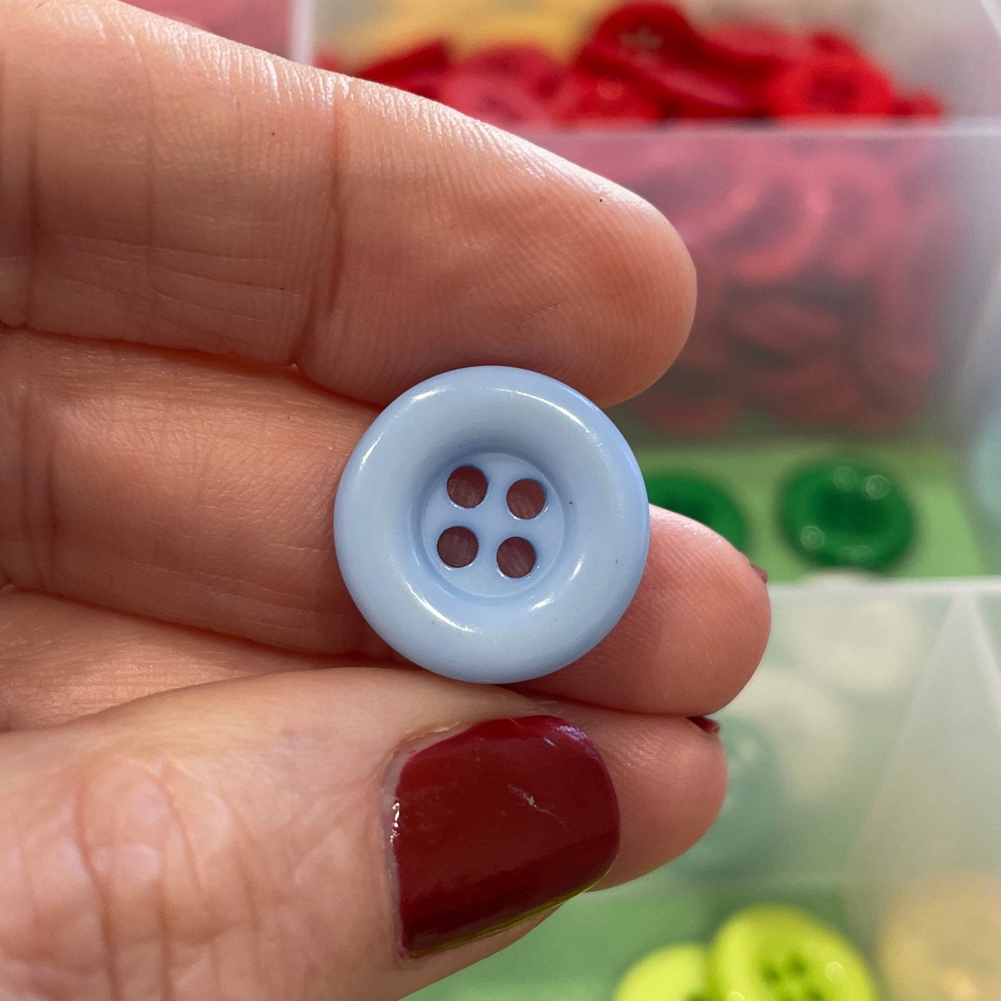 Hand holding a white button with four holes in front of a colorful button collection.