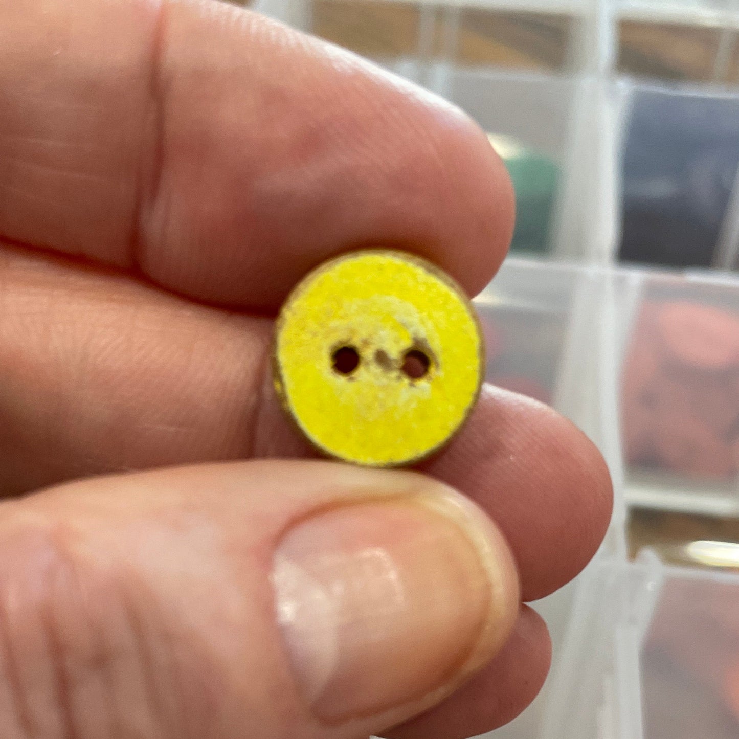 Hand holding a yellow button with a clear container of buttons in the background