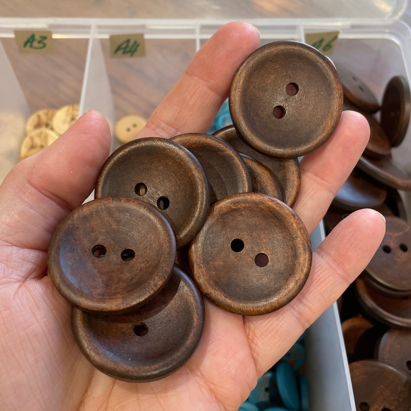 Hand holding brown buttons with a container of buttons in the background