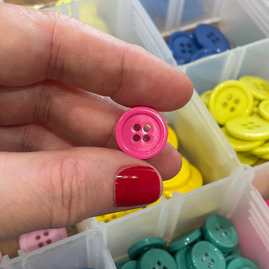 Hand holding a pink button with a container of colorful buttons in the background