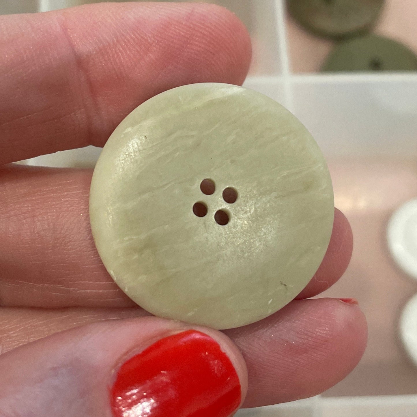 Hand holding a light-colored button with a blurred background of button collection