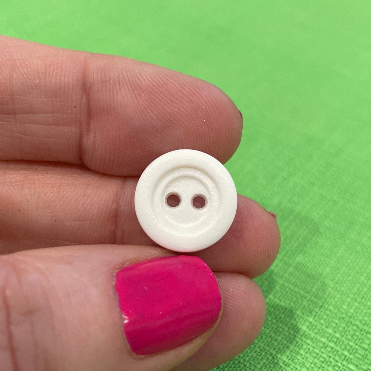White button held between fingers against a green background