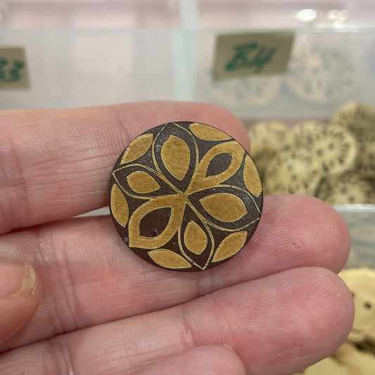 Hand holding a decorative button with a floral pattern in front of a container of assorted buttons.