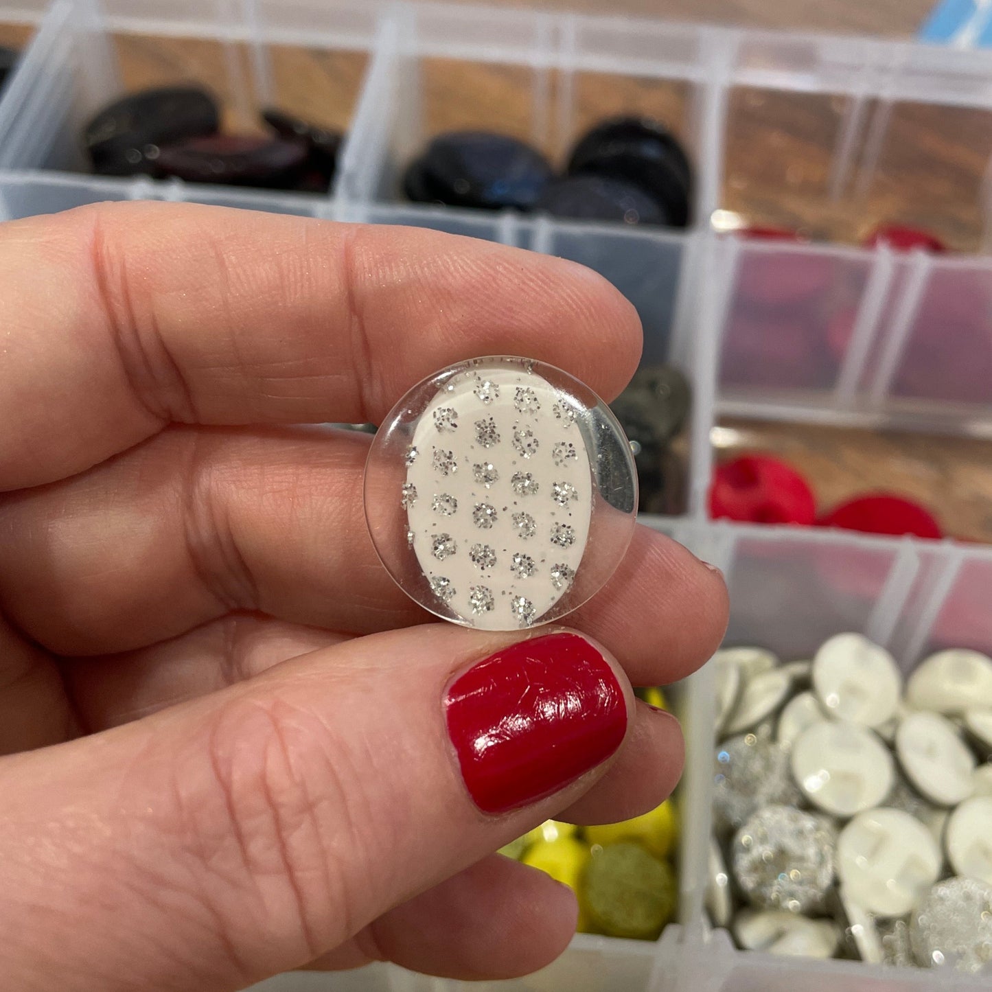 Hand holding a button with rhinestones in front of a container of various buttons.