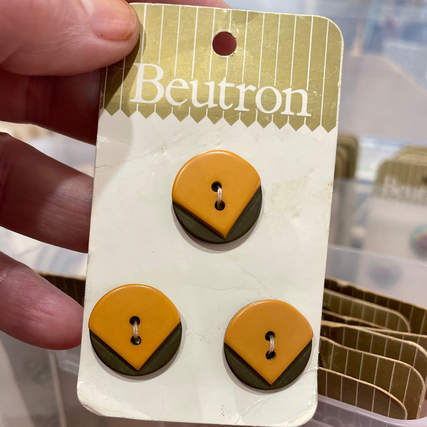 Pair of buttons on a branded card held by a hand.