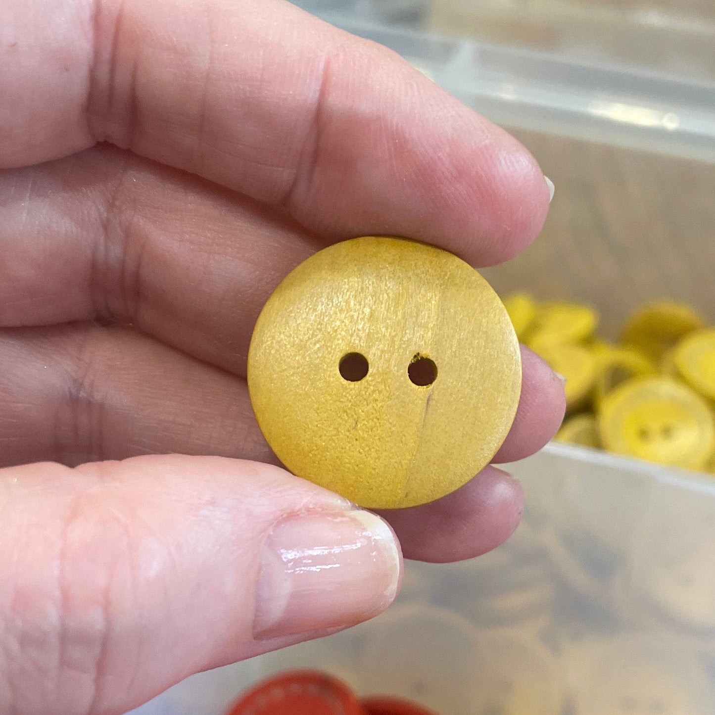 Hand holding a yellow button with a container of red buttons in the background