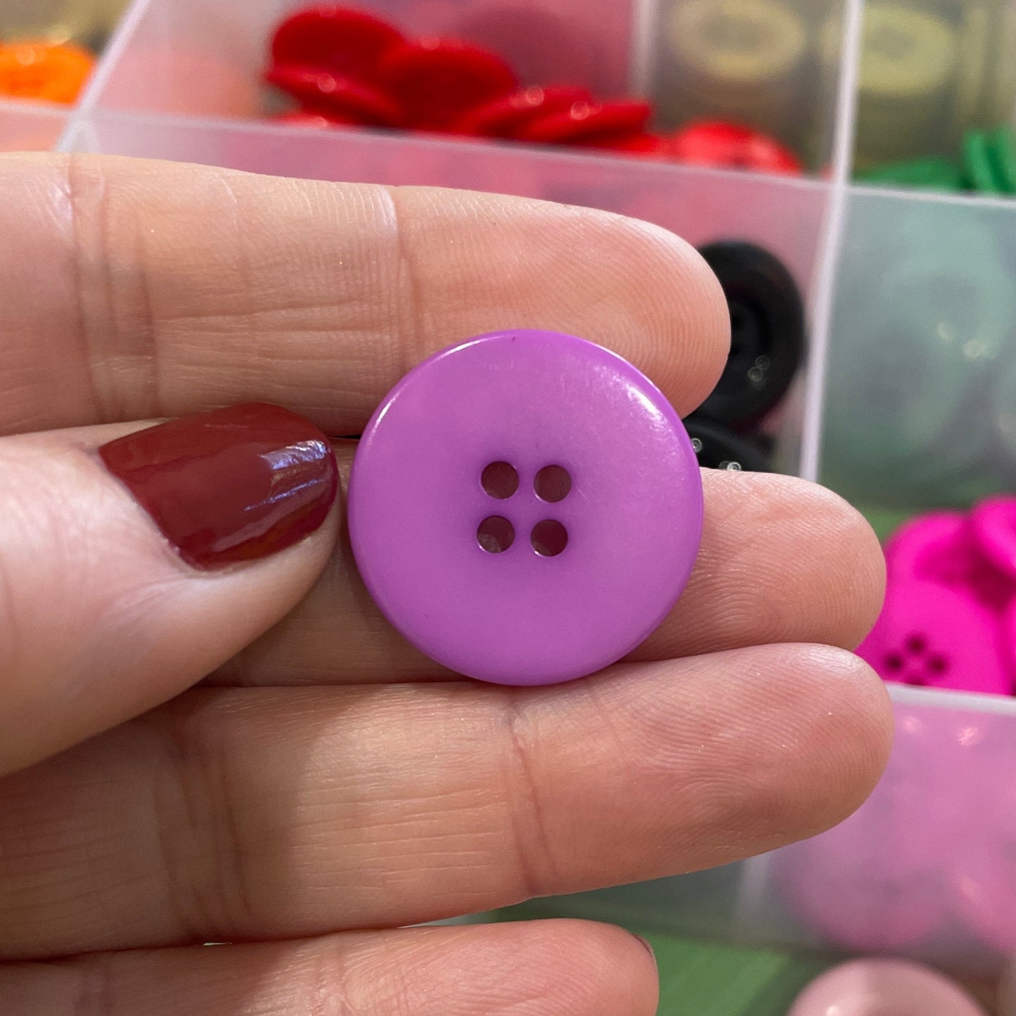 Hand holding a purple button with a clear container of buttons in the background