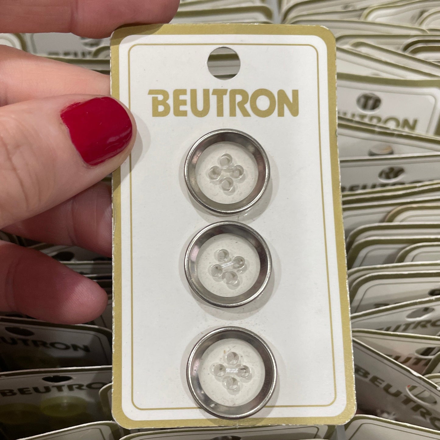 Three buttons on a BEUTRON card held by a hand with red nail polish.