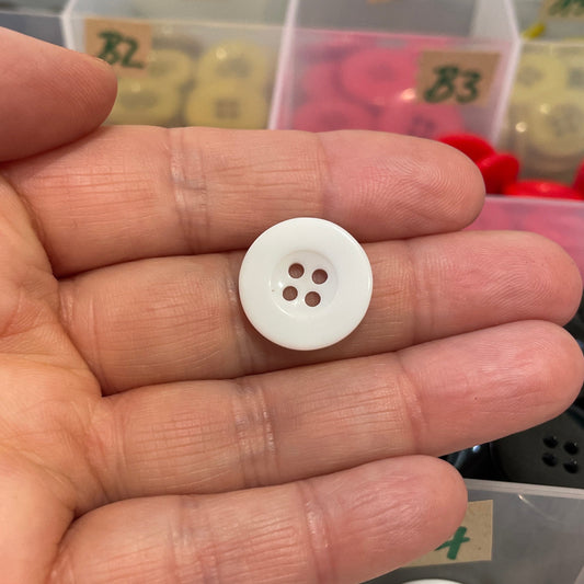 White button held between fingers with a container of buttons in the background