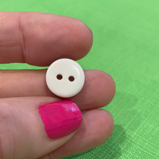 White button held between fingers against a green background