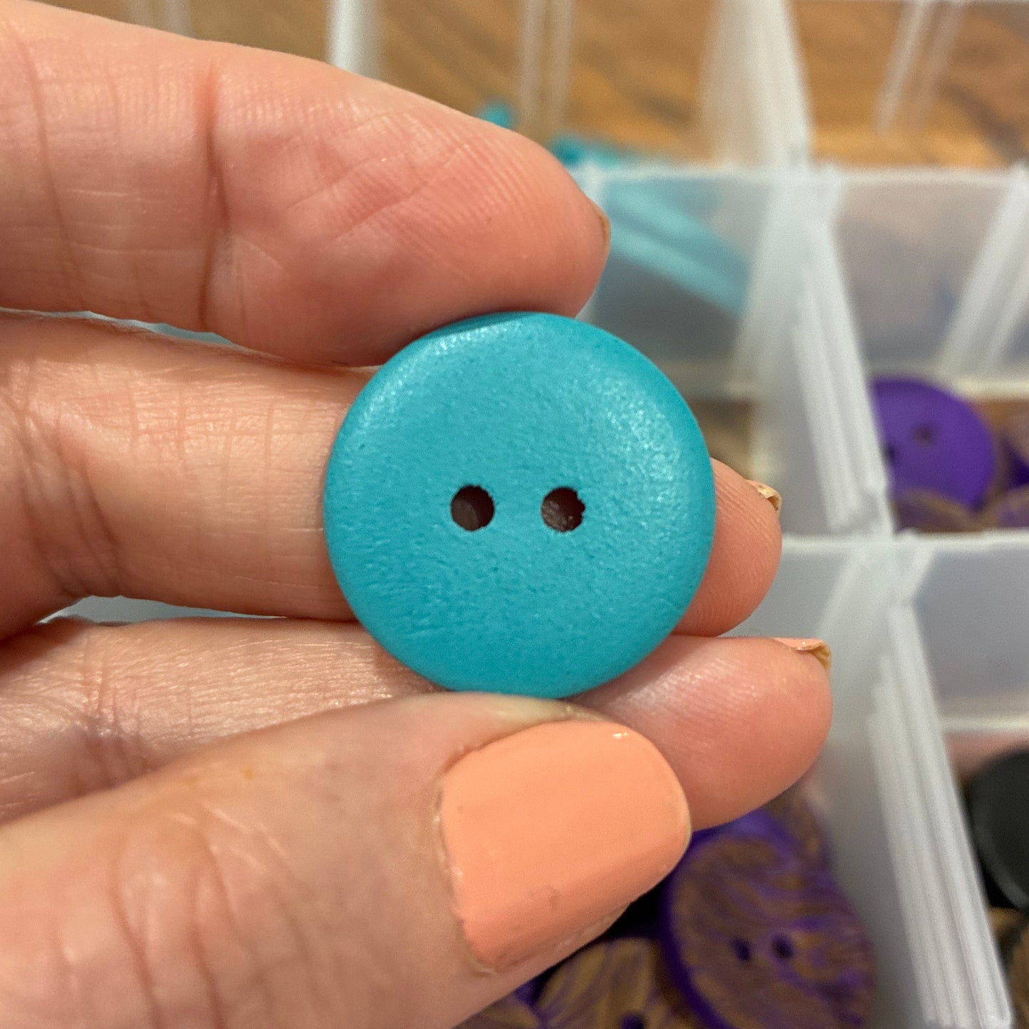 Hand holding a blue button with a container of buttons in the background