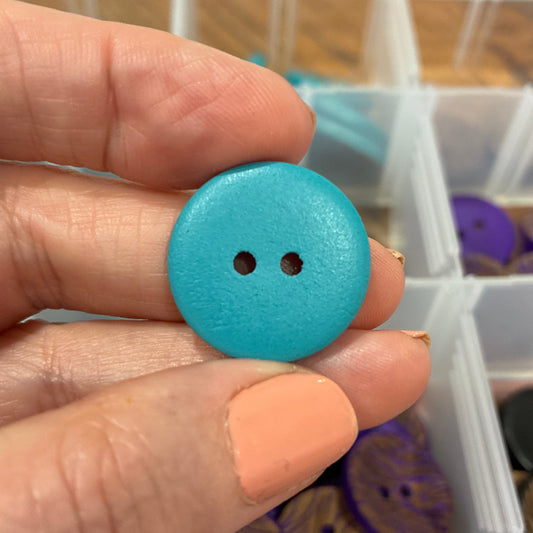 Hand holding a blue button with a container of buttons in the background