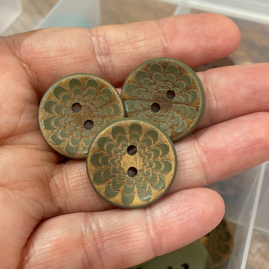 Hand holding three decorative buttons with a clear container of more buttons in the background