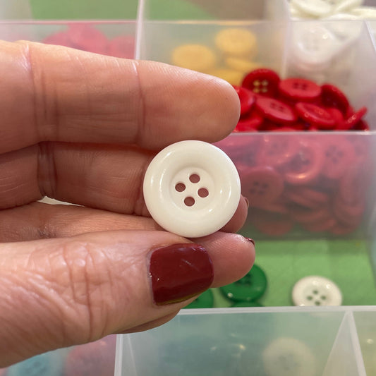 Hand holding a white button with a container of colorful buttons in the background