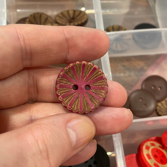Hand holding a decorative button with a clear container of assorted buttons in the background