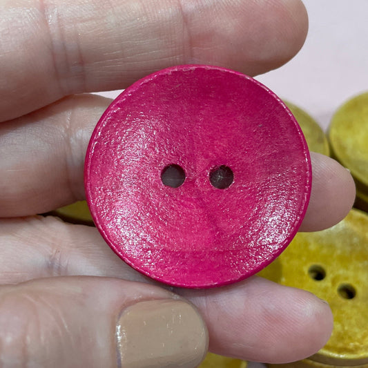 Hand holding a pink button with other buttons on a light surface