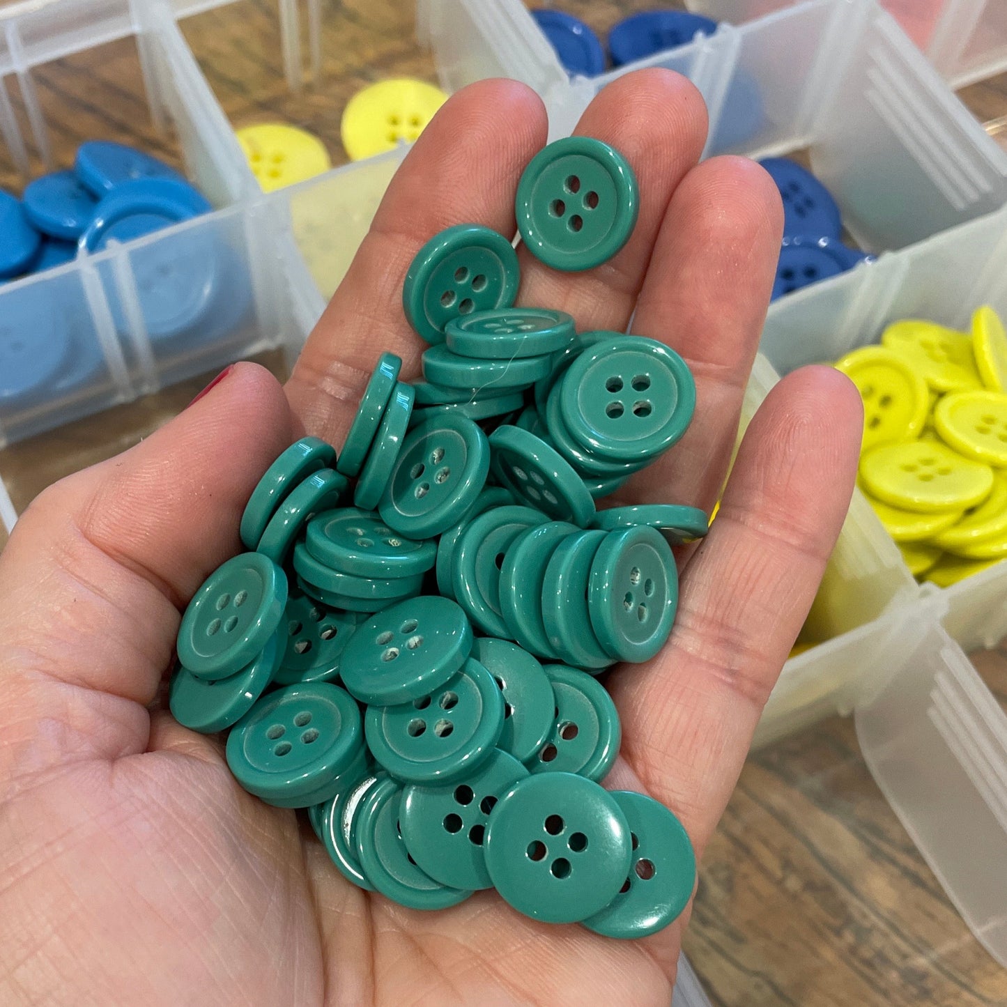 Hand holding green buttons with a container of assorted buttons in the background