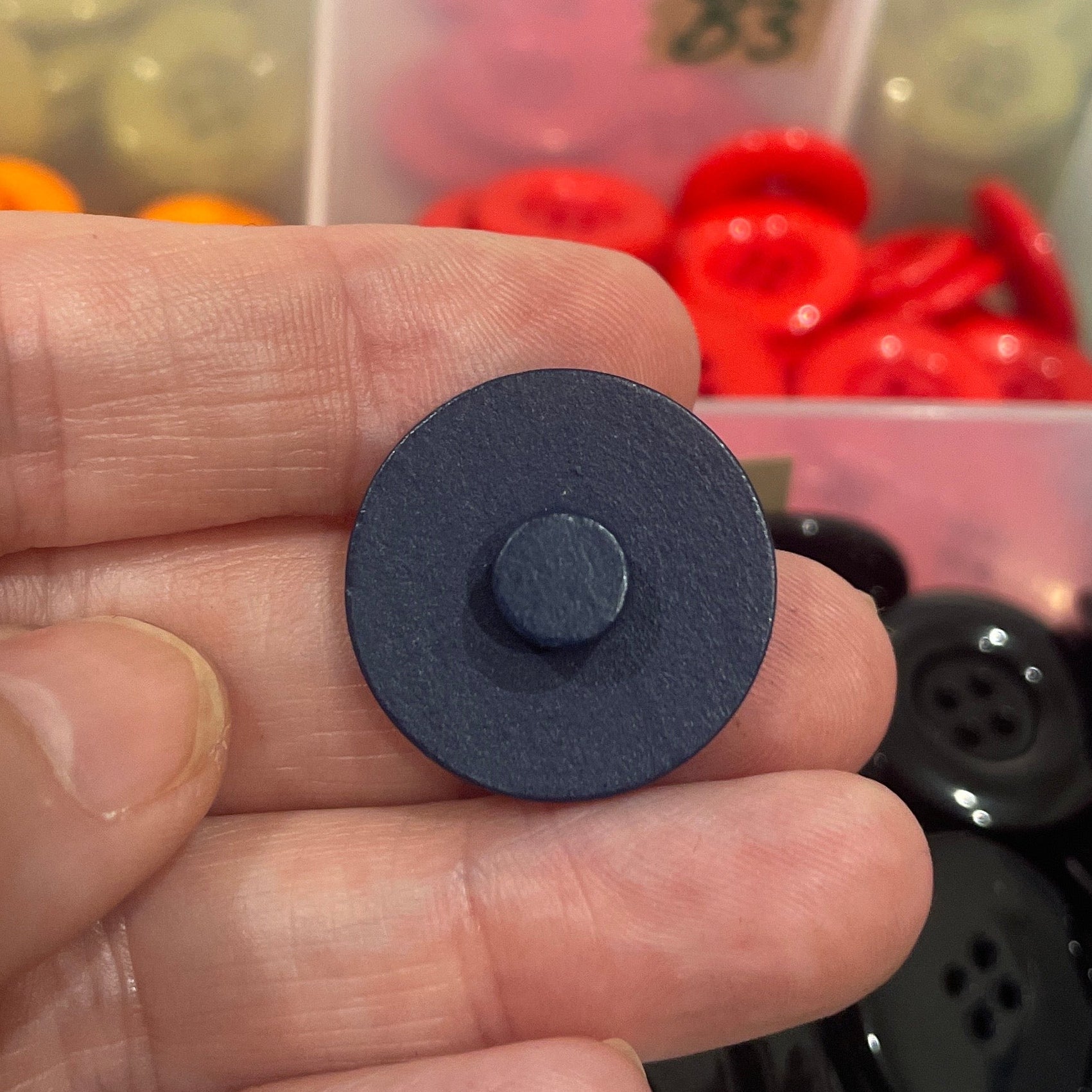 Hand holding a blue button with a colorful assortment of buttons in the background