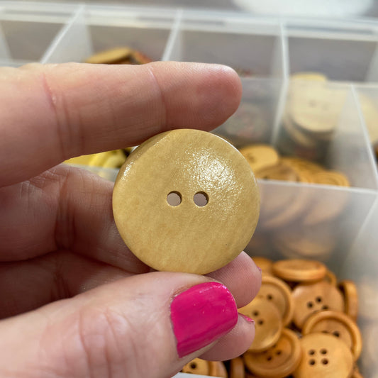 Hand holding a wooden button with a blurred background of button containers.