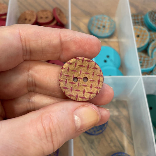 Hand holding a wooden button with a clear container of assorted buttons in the background