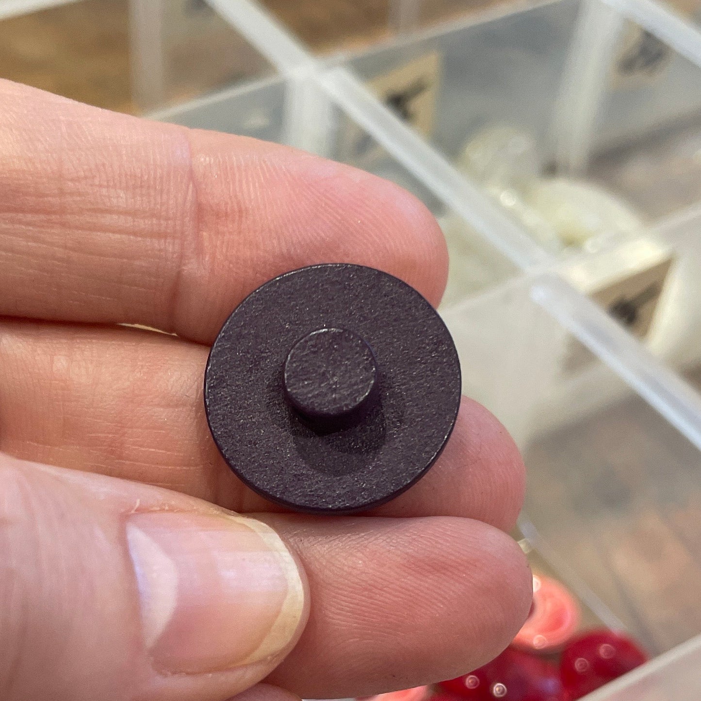 Hand holding a small dark brown button with a blurred background of a button collection.