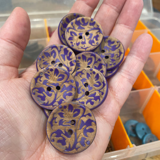 Hand holding purple and gold patterned buttons with a blurred background